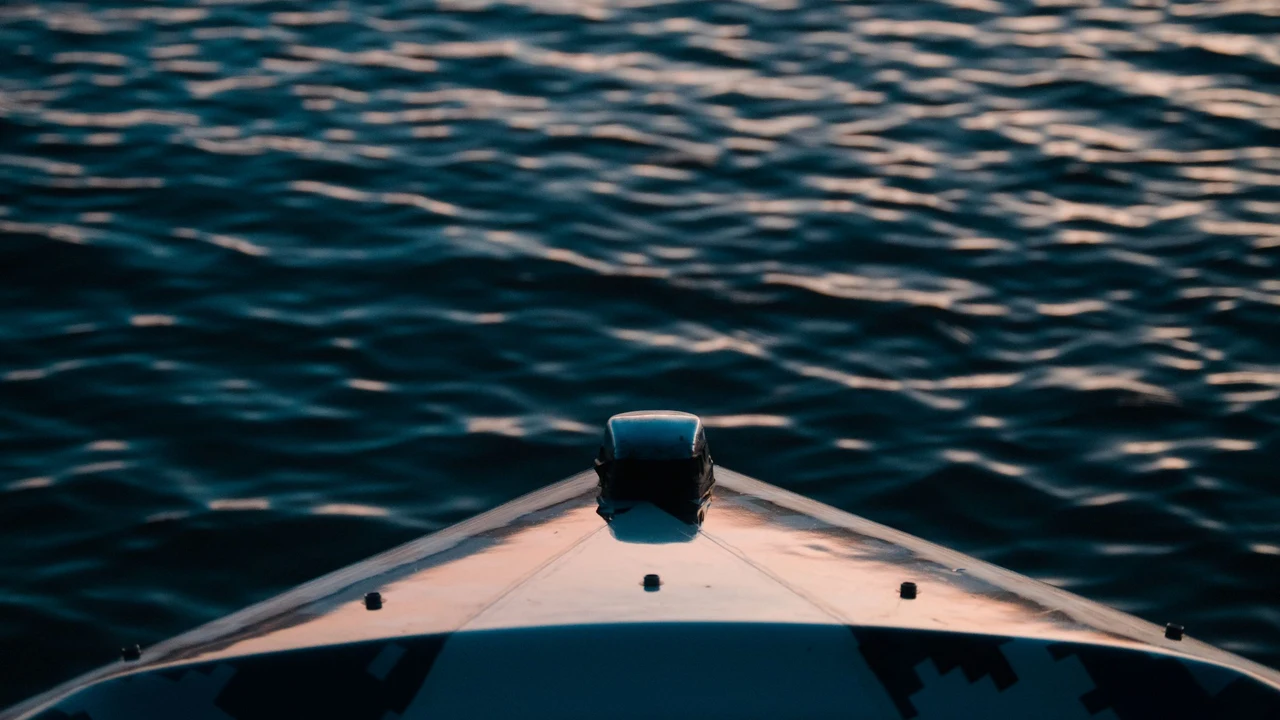 La proue d’un bateau glisse sur une eau sombre où s’accrochent les premiers reflets du jour, personne dans le cadre.
