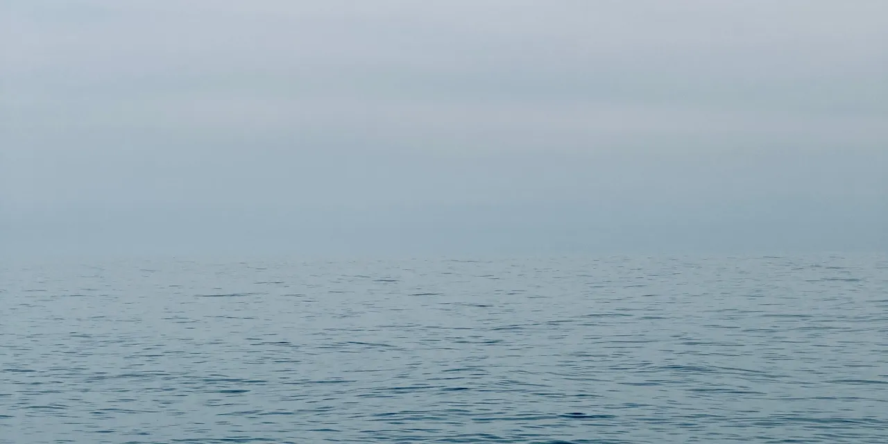 Une mer calme et douce au petit matin, une brume légère posée sur l’horizon.
